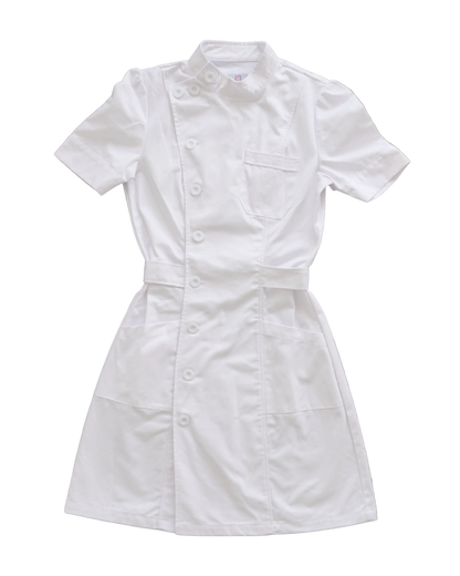 A white short-sleeve nurse scrub dress with a button front, chest pocket, and waist tie, laid flat on a textured gray concrete background.